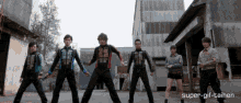 a group of people are standing in front of a building with super-gif-tainen written on the bottom right