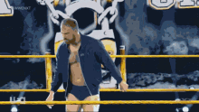 a man in a blue jacket stands in a wrestling ring with the letters wwe next behind him