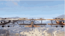 a group of planes are flying over a desert landscape with mountains in the background