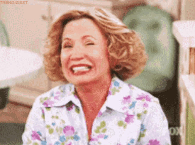 a woman wearing a floral shirt is laughing with her eyes closed .