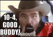a man in a cowboy hat is talking on a cell phone and says `` good buddy enroute '' .