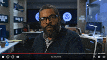 a man with glasses and a beard looks at the camera while playing a video called war of the worlds