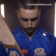 a man holding a cricket bat in front of a mumbaiindians.com logo