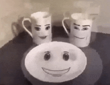 two mugs with faces drawn on them are sitting next to a plate with a smiley face drawn on it .