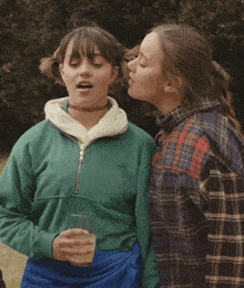 a woman kissing another woman on the cheek while holding a glass