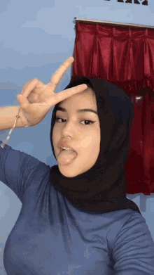 a woman wearing a black hijab is making a peace sign
