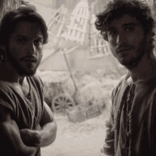 a man with a beard stands next to another man with curly hair