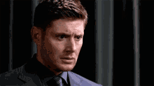a man in a suit and tie is looking at the camera with a sad look on his face .