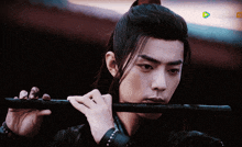a man with long hair is playing a flute in front of a screen that says ' chinese '