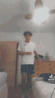 a young man in a white shirt and blue shorts is standing in a bedroom