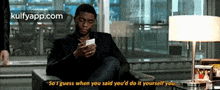 a man is sitting in a chair looking at his phone and saying so i guess
