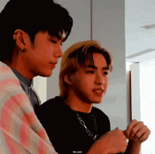 two young men are standing next to each other in a room and looking at each other .