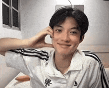 a young man wearing a white adidas shirt is sitting on a bed with his hand on his face .