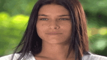 a woman with long dark hair and a white shirt looks at the camera
