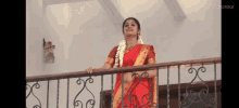 a woman in a red saree is standing on a balcony holding onto a railing .