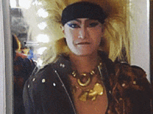 a woman wearing a black headband and a gold necklace stands in front of a mirror .