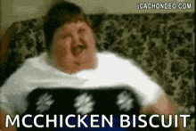 a fat man is sitting on a couch eating mcchicken biscuits .