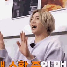 a young man with blonde hair is giving a high five while wearing a white sweater .