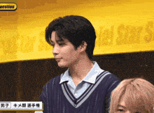 a man in a sweater stands in front of a sign that says question