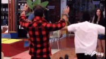 a man in a plaid shirt is dancing in a room with other people .