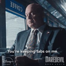a man in a suit and tie says " you 're keeping tabs on me " while holding a mug