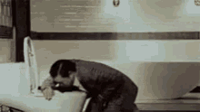 a man in a suit is washing his hands in a sink in a bathroom .