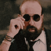a man with a beard is wearing a suit and tie and round sunglasses