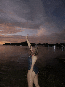 a woman in a swimsuit stands in front of a body of water giving a thumbs up