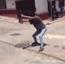 a man in a black shirt and blue jeans is squatting on the sidewalk