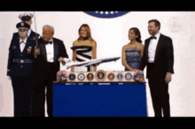 a man in a tuxedo holds a model airplane in front of a group of people