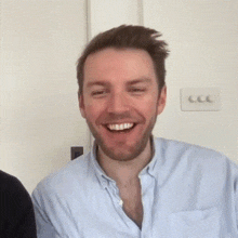 a man with a beard wearing a blue shirt is smiling .
