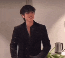 a man in a black suit is standing next to a table with green onions and a kettle .