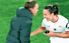 a man and a woman are standing on a soccer field and the woman is wearing a white jersey with a spider on it