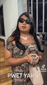 a woman wearing sunglasses and a dress is holding a pink purse and talking to someone .