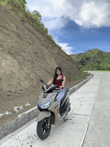 a woman sits on a honda scooter on a concrete road