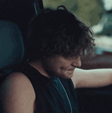 a man with curly hair is sitting in a car with his eyes closed