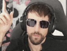 a man with a beard and sunglasses is wearing headphones and giving a thumbs up .