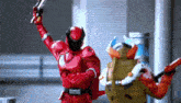 a red superhero is holding a gun while standing next to another superhero .