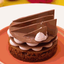 a chocolate cake with whipped cream and chocolate slices on an orange plate