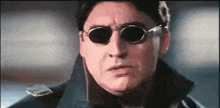 a man wearing sunglasses and a black coat is making a funny face .