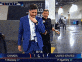 a man in a blue suit is being escorted by a man in a black shirt during a united states vs canada match