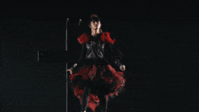 a woman in a red and black dress stands in front of a fireworks display