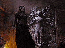 a woman in a black dress stands in front of a statue of a woman