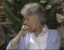 a woman with gray hair and a blue sweater is biting her nails while sitting outside .
