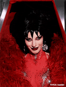 a woman in a red dress and black wig is sitting in a coffin