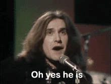 a man with long hair singing into a microphone with the words oh yes he is behind him