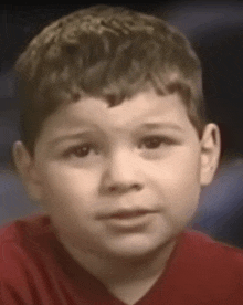 a young boy is wearing a red shirt and looking at the camera