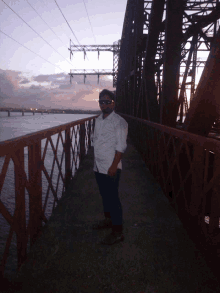 a man in a white shirt stands on a bridge over a body of water