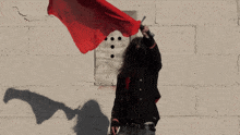 a man in a black jacket holds a red flag in front of a brick wall