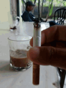 a person is holding a cigarette in front of a glass of coffee